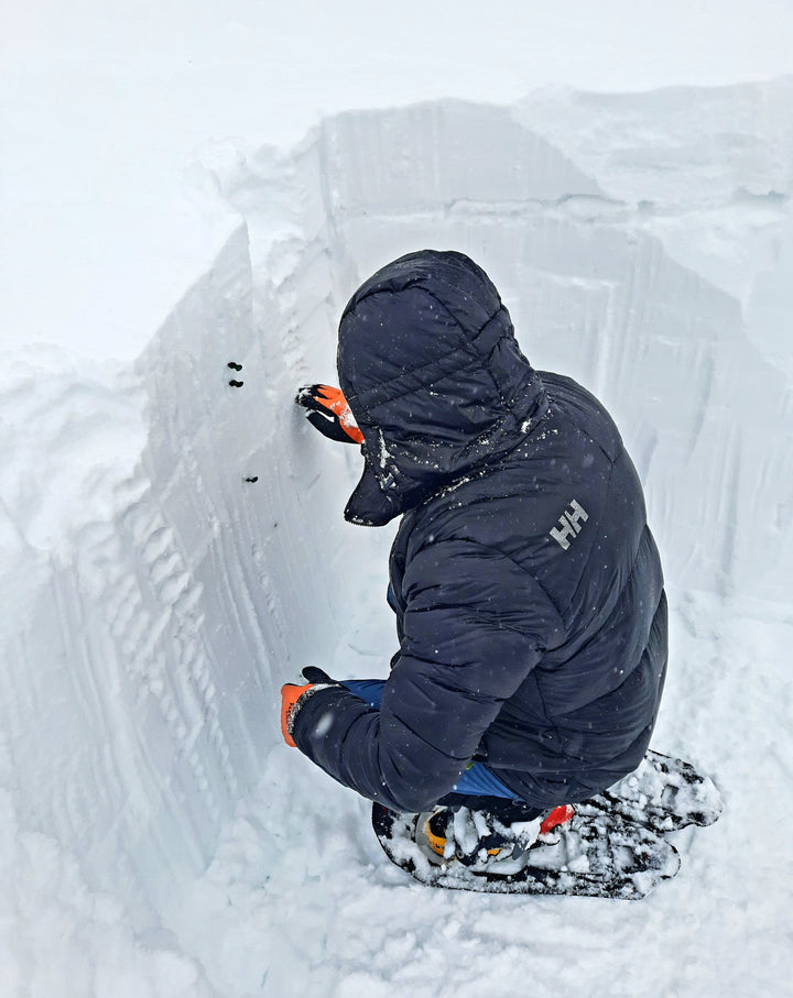 A student wearing snowshoes performs a hand harness test to evaluate snowpack layers.