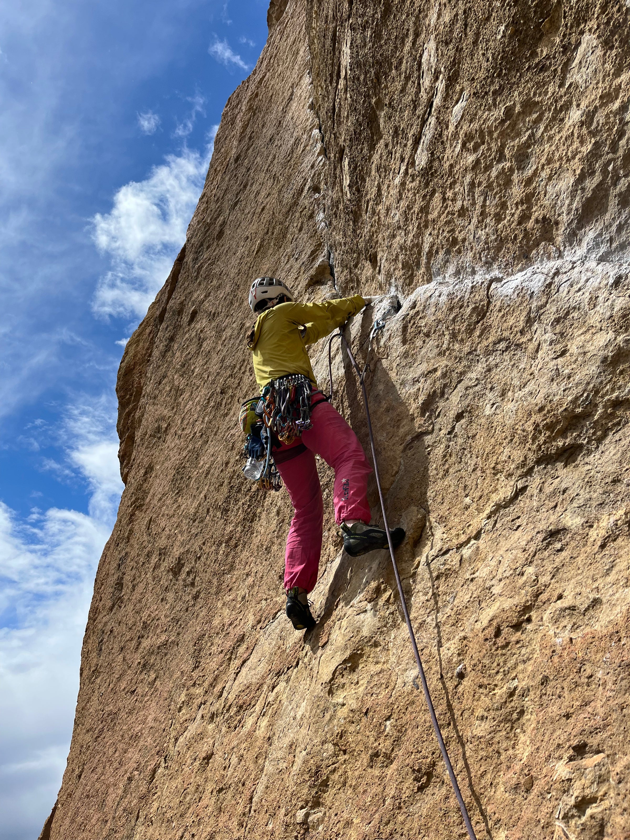 A person in bright colors climbs along a chalk covered rail looking for a good stance to place protection.