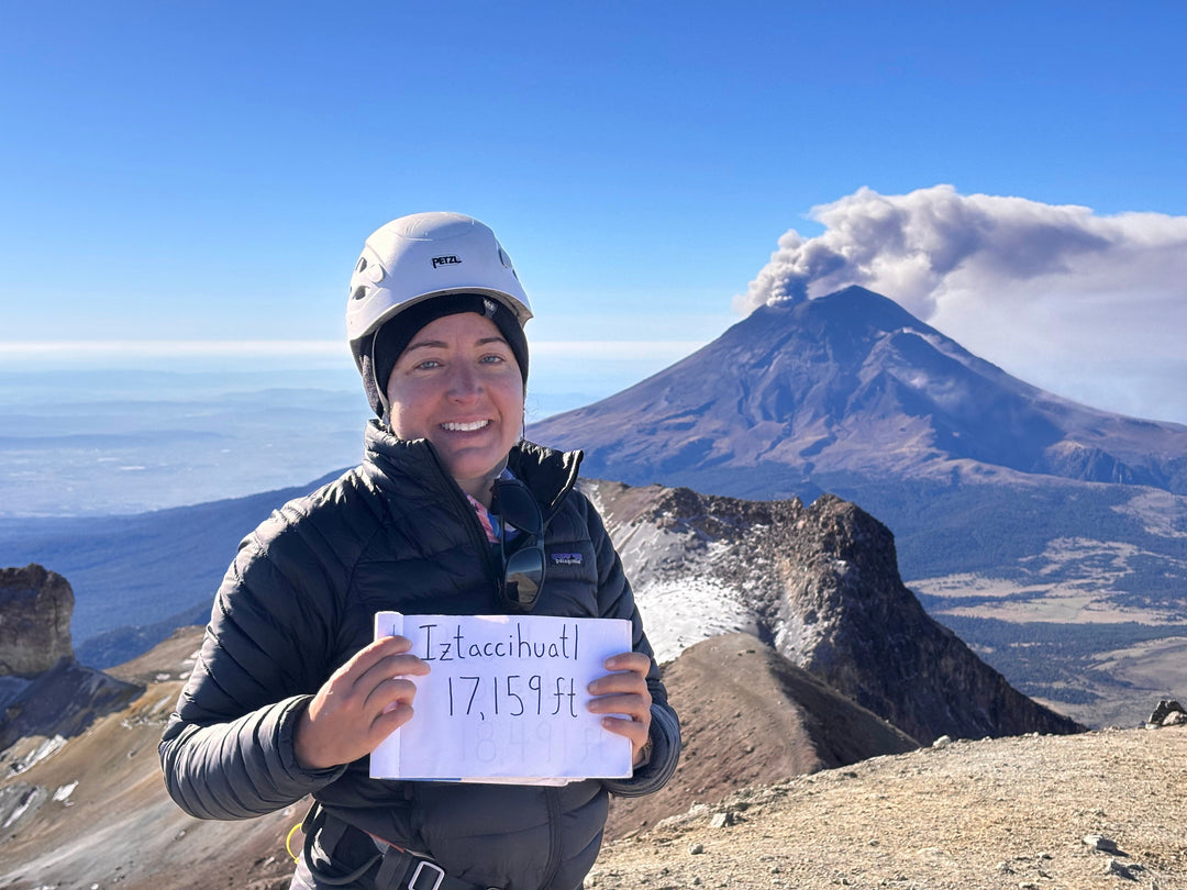 smiling woman holding sign at summit of mountain