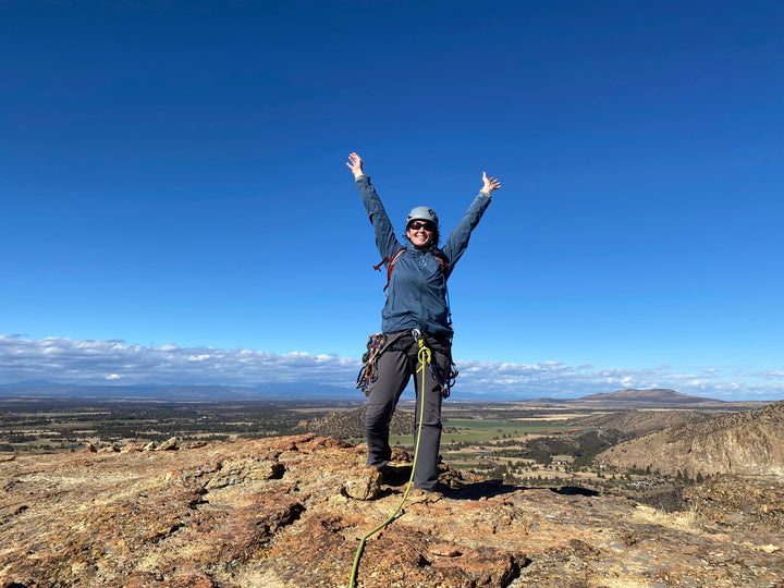 A climber celebrates the completion of her multi-pitch climb at Smith Rock with her hands in the air.