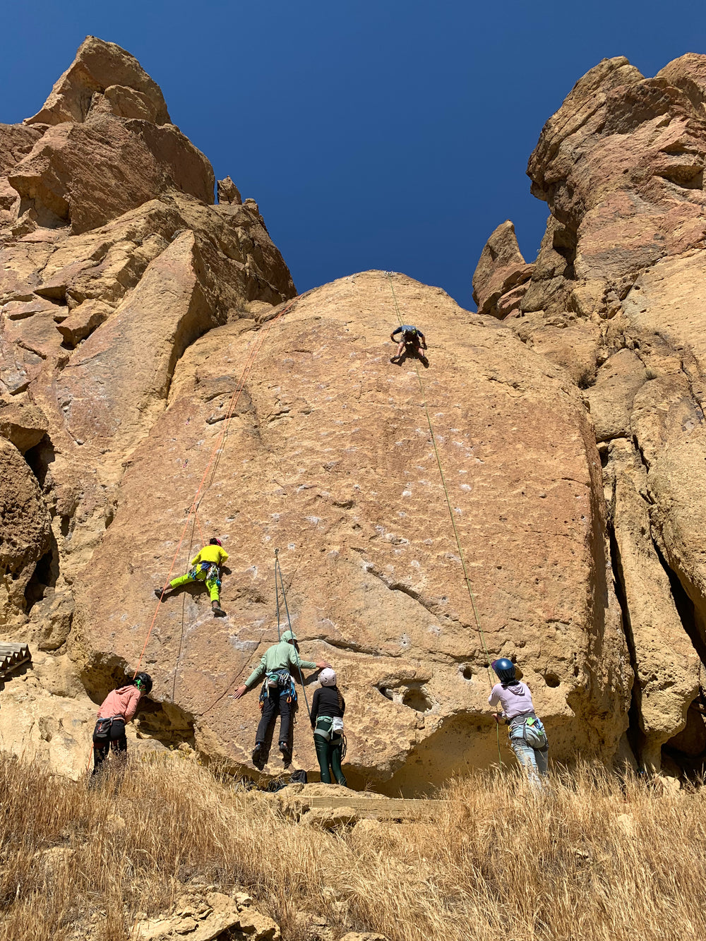 Climbers belay each other on a smooth rock with chalk marks at Smith.