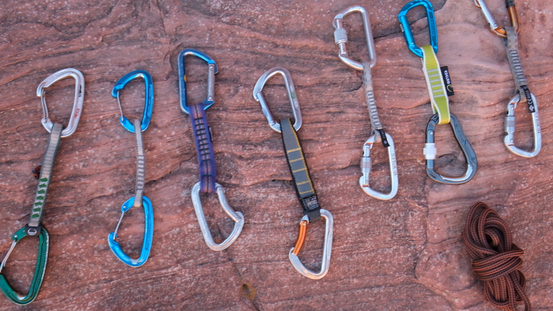 Several belay devices laid out in a row on top of reddish rock